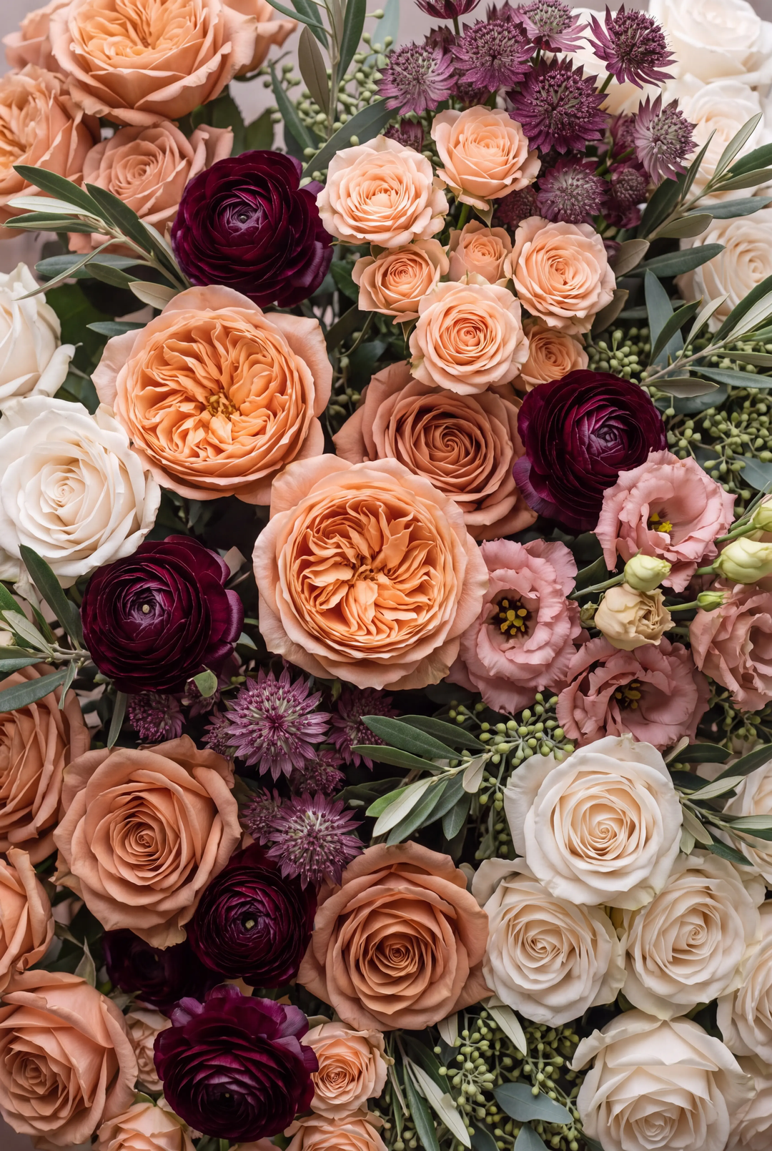 Overhead close-up of a dense floral arrangement in terracotta, peach, cream, and burgundy — garden roses, ranunculus, lisianthus, and astrantia.